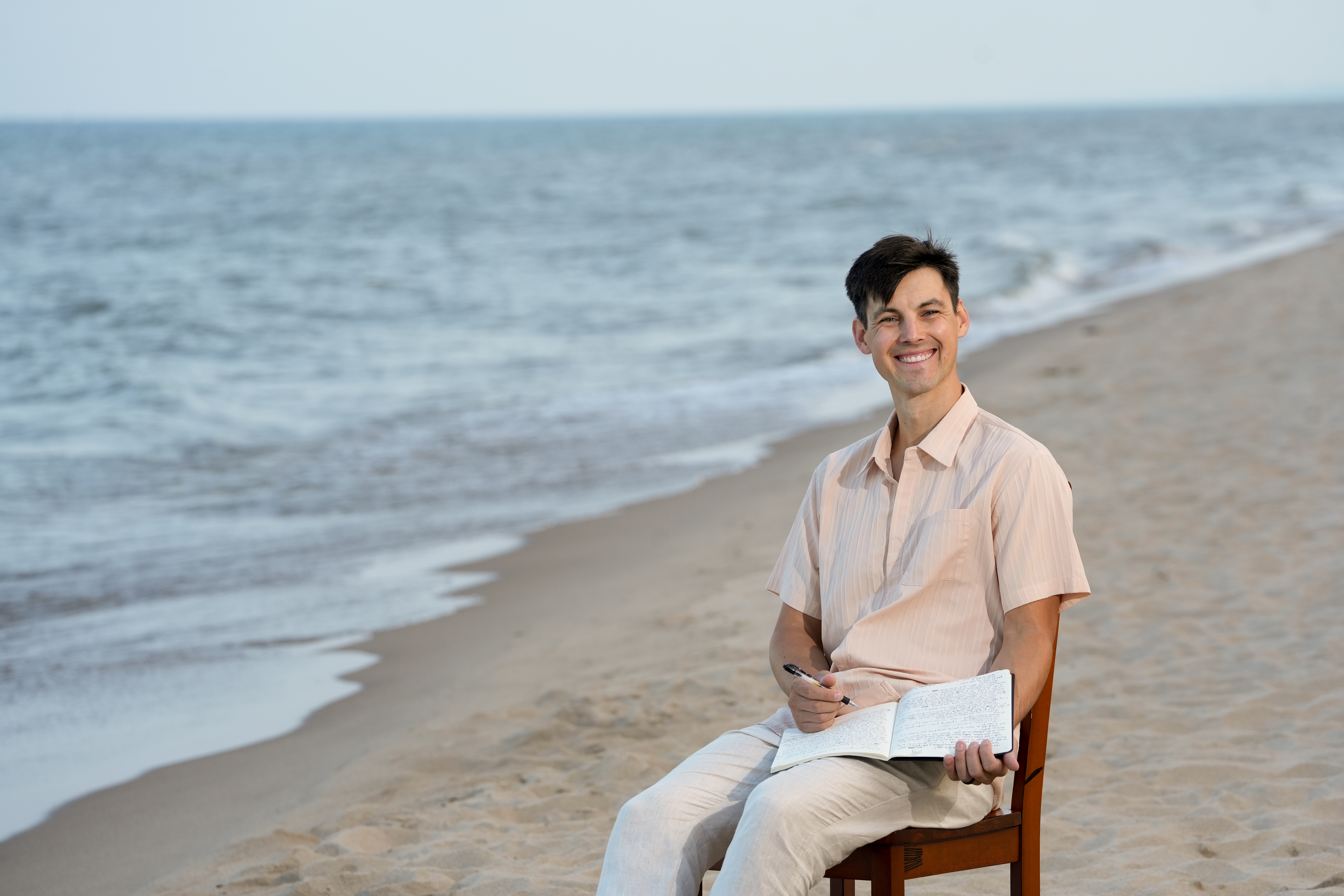 Michael Brooks seated on the beach with a notebook in his lap.